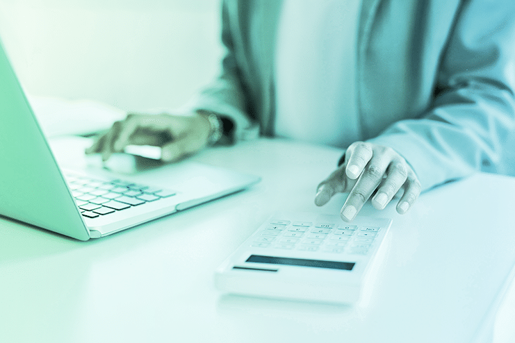 close up picture of a man at his desk, working on a laptpop and a calculator.