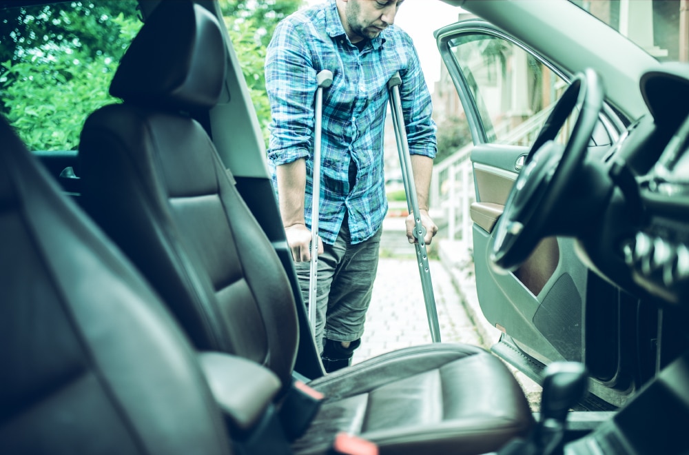 A man on crotches gets into a car.