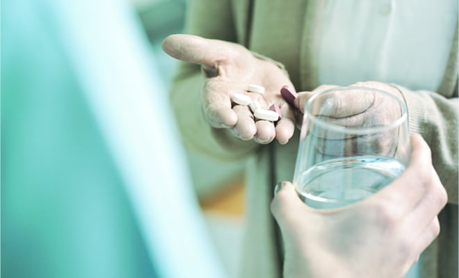 Close up of a person holding some pills in their hand and another offeing a glass of water.