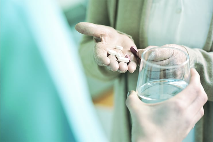 Close up of a person holding some pills in their hand and another offeing a glass of water.